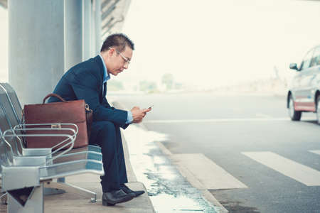 Elegant businessman texting while sitting at the bus stop in the airportの写真素材