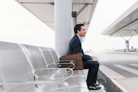 Businessman sitting on the chair at the airport bus stop and looking away, side view