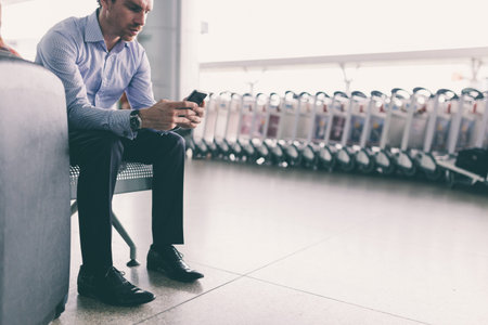 Young Caucasian businessman texting while sitting at the airport terminalの写真素材