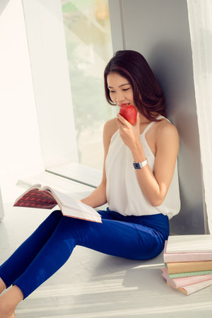 Vietnamese girl reading a book and eating fresh appleの写真素材
