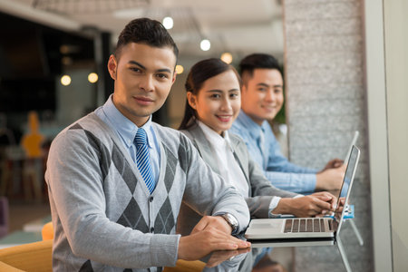 Portrait of handsome businessman and his colleagues sitting in the cybercafe and looking at the cameraの写真素材