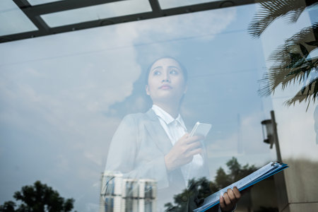 Vietnamese business lady with a cellphone looking out of the windowの写真素材