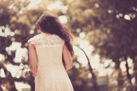 Lady in a lace dress with flowers in her hands, rear viewの写真素材