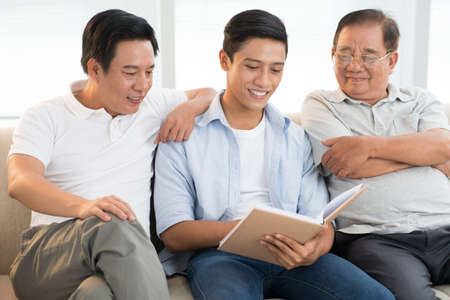 Grandfather, son, and grandson reading a book togetherの写真素材