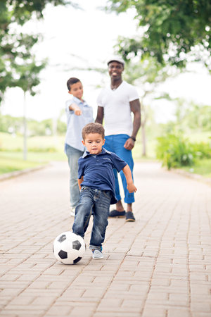 Little boy kicking soccer ball while his father and brother watching in the backgroundの写真素材