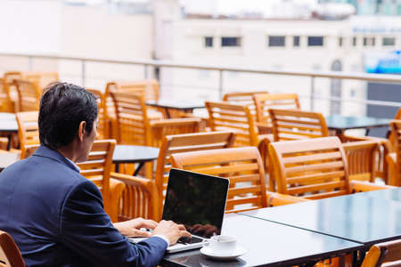 Businessman sitting in the cafe and working on laptop, rear viewの写真素材