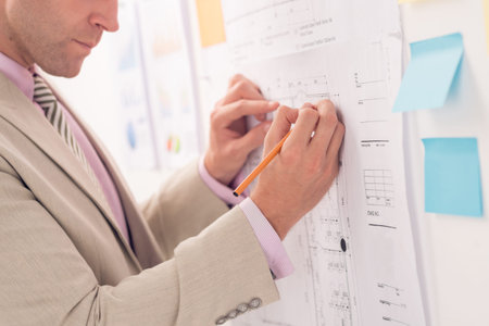 Cropped image of serious engineer improving blueprint of the houseの写真素材