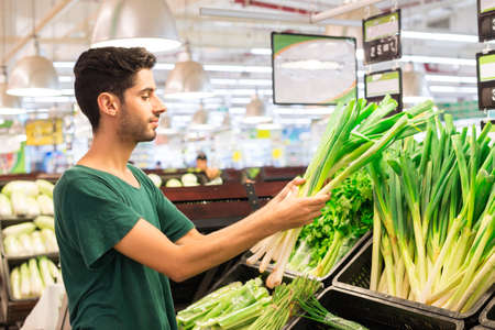 Hispanic man buying leek in the supermarketの写真素材