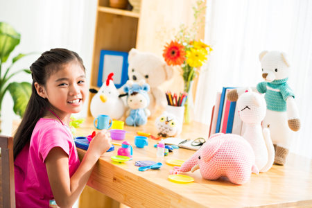 Cheerful little girl playing with toy dish set and knitted toy animals