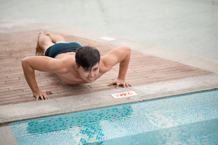 Young man doing push-ups by the swimming poolの写真素材