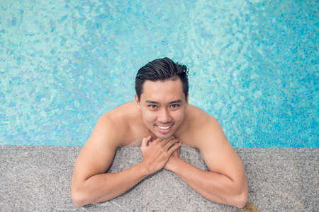 Portrait of handsome Vietnamese man relaxing in the swimming pool, view from aboveの写真素材