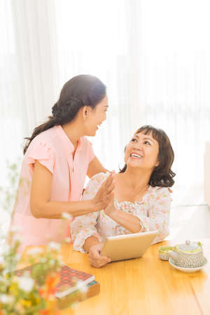 Aged woman playing on tablet getting high five from her friendの写真素材