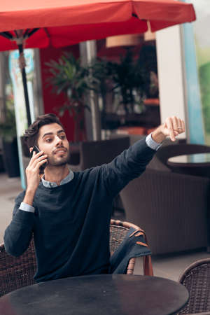 Handsome man talking on the phone and asking for waiterの写真素材
