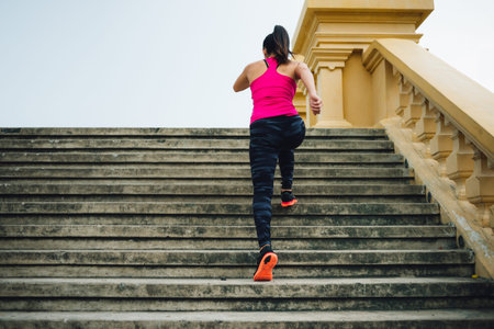 Rear view of female athlete running up the stairsの写真素材