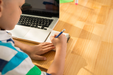 Boy writing something in his notepad, view over the shoulder
