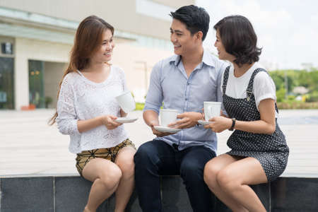 Cheerful young people talking and drinking tea outdoorsの写真素材