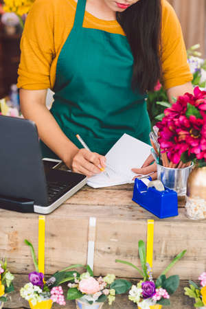 Worker at cash desk writing in notepadの写真素材