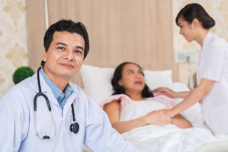 Portrait of mature doctor and nurse taking care of patient in backgroundの写真素材