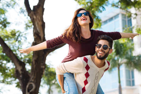 Cheerful young woman with her arms outstretched enjoying piggyback rideの写真素材