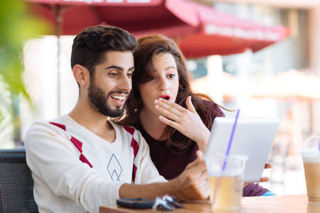Shocked young couple watching something on the digital tablet while sitting in the cafeの写真素材
