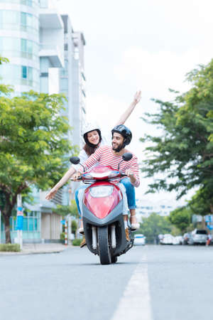 Happy excited couple riding a motor scooter, the body of the scooter has been changed digitallyの写真素材