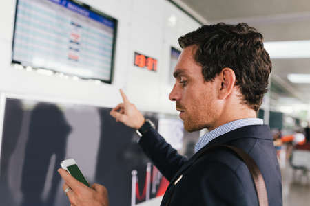 Businessman with a cellphone and pointing at the airline scheduleの写真素材