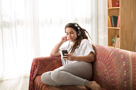 Teenage girl with dreadlocks listening to the music on headphones at homeの写真素材