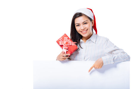 Smiling girl with a Christmas gift pointing at the blank banner