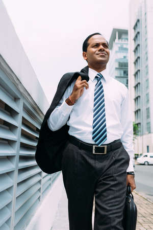 Businessman walking along the street with jacket over his shoulderの写真素材