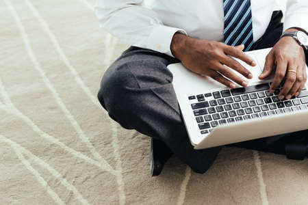 Unrecognizable businessman sitting on the floor and working on laptop, selective focusの写真素材