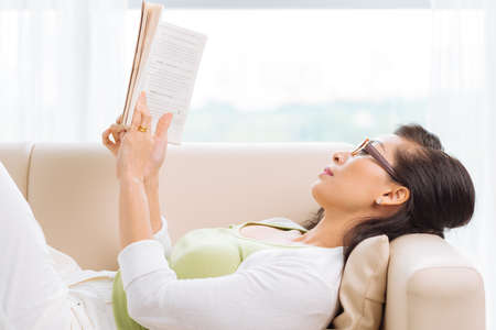 Woman lying on the sofa and reading a book, side viewの写真素材