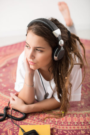 Portrait of young girl lying on the floor and listening to the musicの写真素材