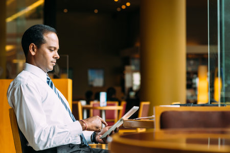 Indian businessman sitting in the cafe and reading news on the digital tabletの写真素材
