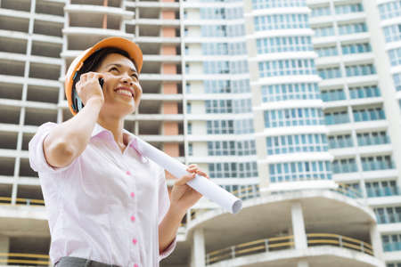 Young arching with a blueprint talking on the phoneの写真素材