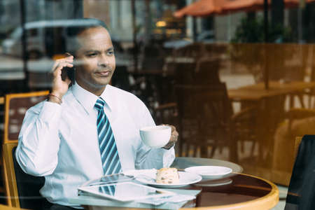 Serious businessman drinking coffee and talking on the phone in the cafeの写真素材