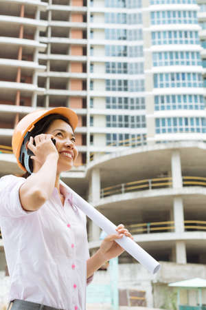 Beautiful woman in a hard hat talking on the phone at the construction siteの写真素材