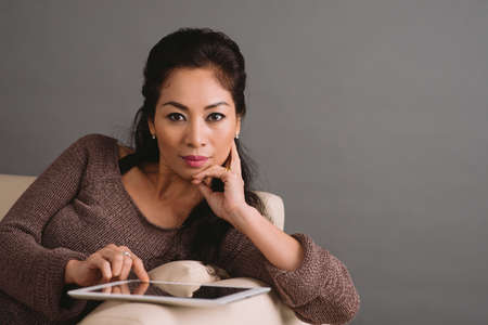 Portrait of gorgeous woman lying on the sofa and using digital tabletの写真素材