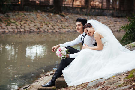 Newly married Vietnamese couple sitting on the bank of the riverの写真素材