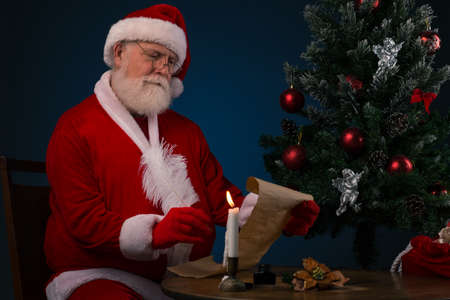 Santa Claus sitting at table and writing on old paper rollの写真素材