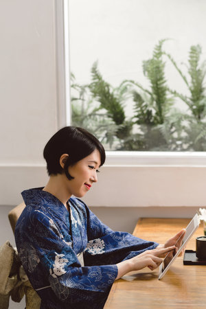 Young Japanese woman in traditional dress using digital tablet at homeの写真素材