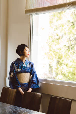 Pensive Japanese woman in kimono looking through the windowの写真素材