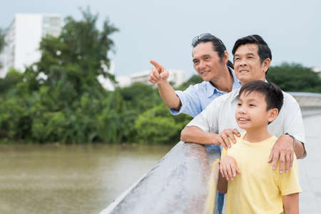 Middle-aged man showing something interesting to his father and son while standing on the bridgeの写真素材