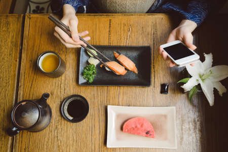 Hands of woman using smartphone while eating sushiの写真素材