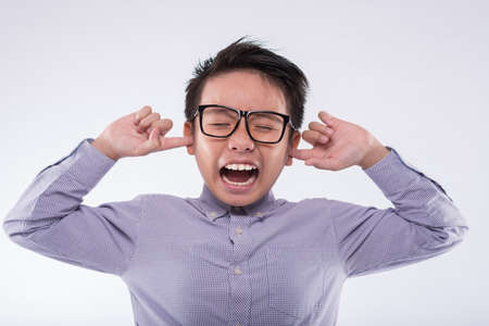 Boy with fingers in his ears closing eyes and screamingの写真素材