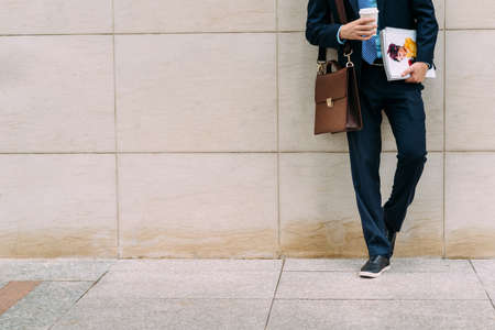 Cropped image of businessman with coffee and documents leaning on the wallの写真素材