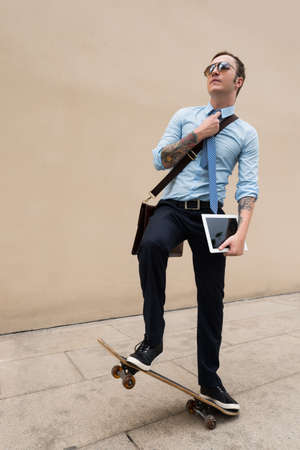 Cool young businessman with a digital tablet balancing on skateboardの写真素材