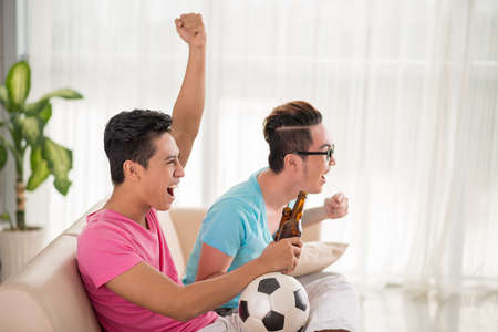 Vietnamese young men sitting on the sofa and supporting favorite soccer teamの写真素材