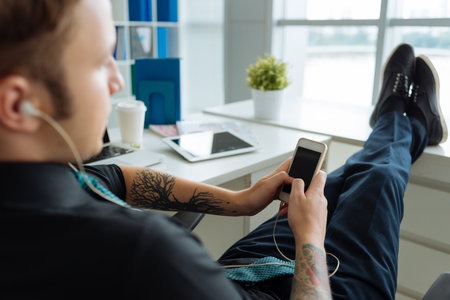 Manager sitting with his legs on the window-sill and text messaging