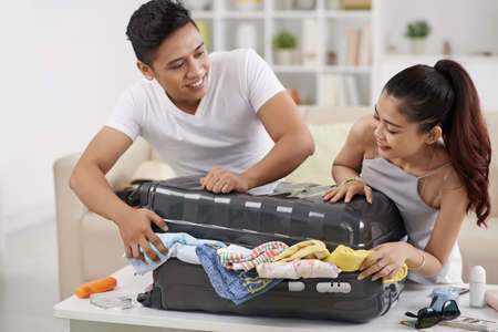Couple trying to close overstuffed suitcaseの写真素材