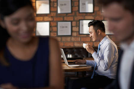 Asian businessman drinking coffee and using laptop in cafeの写真素材